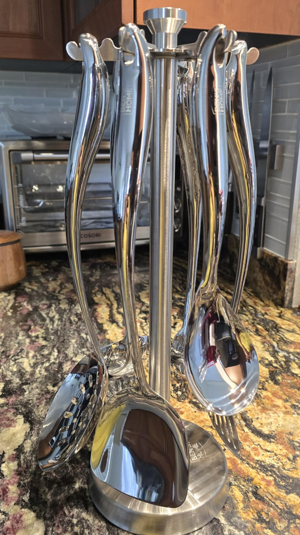 Set of silver kitchen utensils in a holder on a marble countertop.